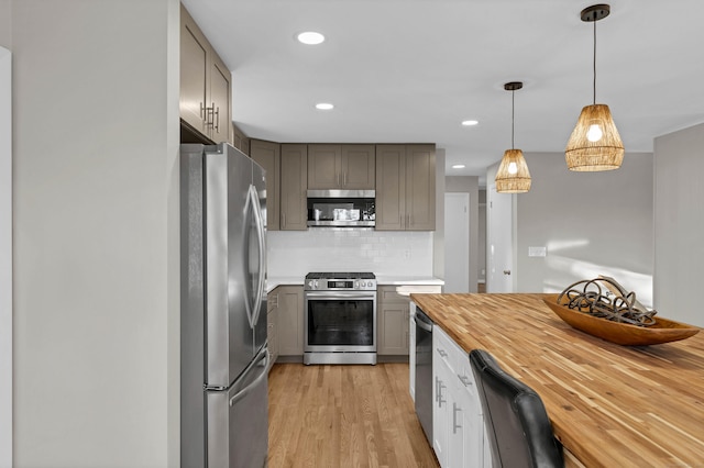 kitchen with gray cabinetry, stainless steel appliances, pendant lighting, decorative backsplash, and light wood-type flooring