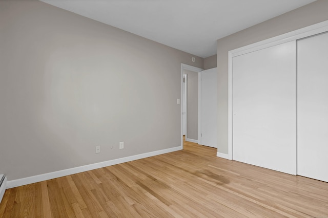 unfurnished bedroom with a closet, light hardwood / wood-style floors, and a baseboard radiator