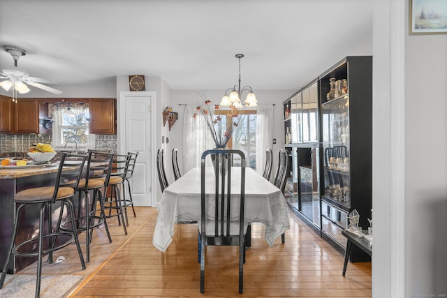 dining space with sink, light hardwood / wood-style flooring, and ceiling fan with notable chandelier