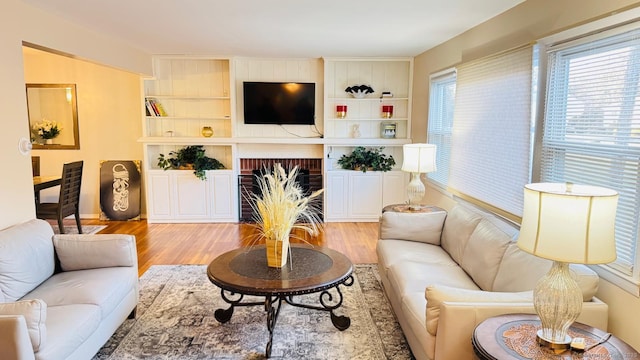 living room featuring built in features, light wood-type flooring, and a brick fireplace