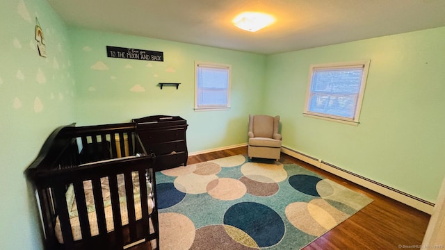 bedroom featuring baseboard heating, a crib, and hardwood / wood-style flooring