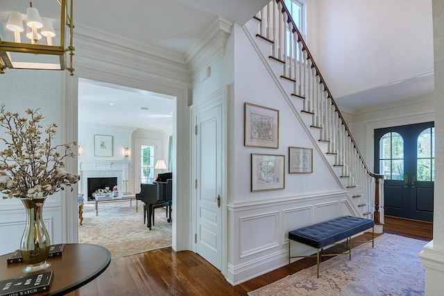 foyer featuring wood-type flooring, french doors, an inviting chandelier, and a premium fireplace