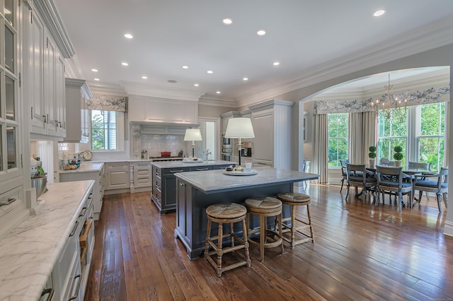 kitchen featuring white cabinetry, backsplash, dark wood-type flooring, a kitchen island, and light stone counters