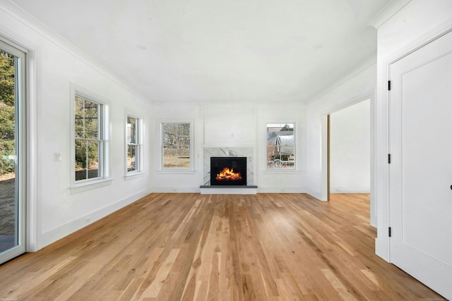 unfurnished living room with ornamental molding, a high end fireplace, and light wood-type flooring