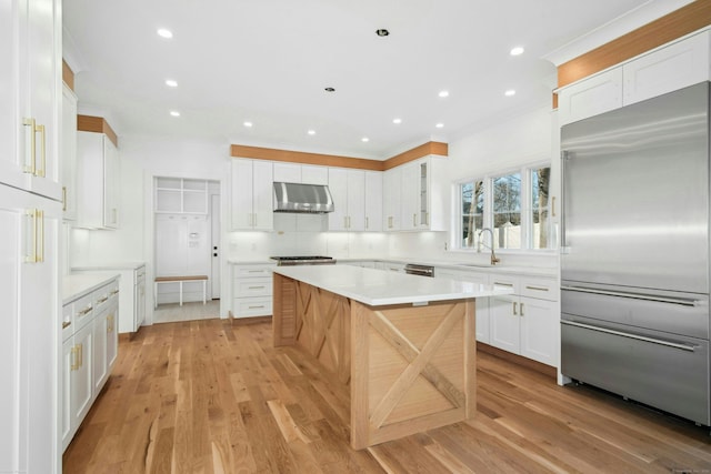 kitchen featuring sink, stainless steel appliances, white cabinets, a kitchen island, and light wood-type flooring