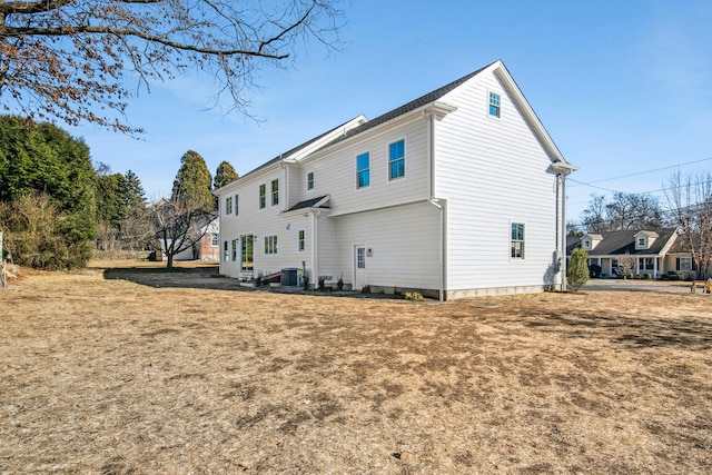 rear view of house with cooling unit and a lawn