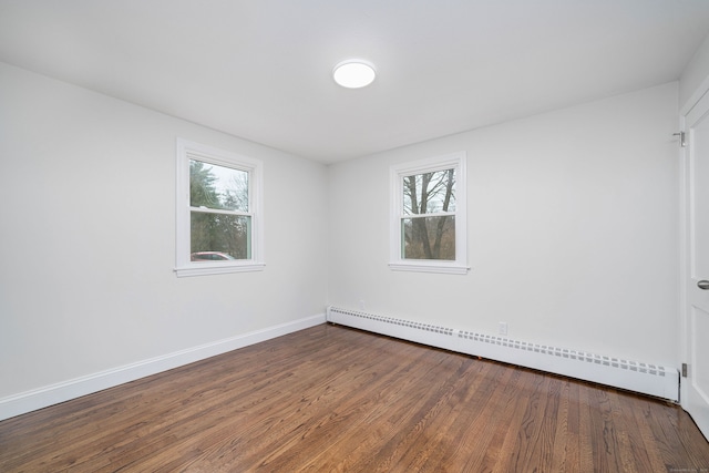 empty room featuring a baseboard heating unit and dark wood-type flooring