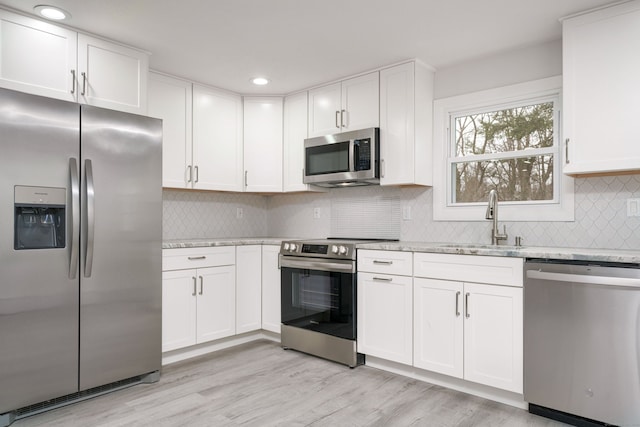 kitchen featuring white cabinetry, stainless steel appliances, light wood-type flooring, light stone counters, and sink