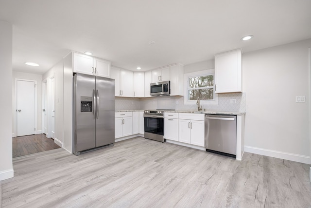 kitchen with tasteful backsplash, white cabinets, stainless steel appliances, and light hardwood / wood-style flooring