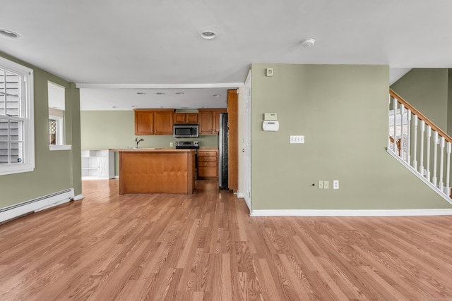 kitchen with appliances with stainless steel finishes, light wood-type flooring, baseboard heating, and a healthy amount of sunlight