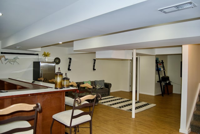 basement with light hardwood / wood-style flooring and stainless steel fridge