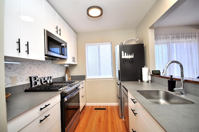 kitchen featuring white cabinets, stainless steel appliances, tasteful backsplash, sink, and light hardwood / wood-style flooring