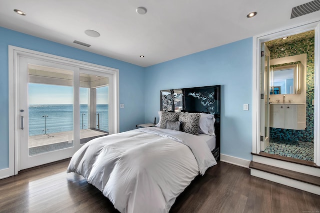 bedroom with connected bathroom, dark hardwood / wood-style floors, access to exterior, and a water view