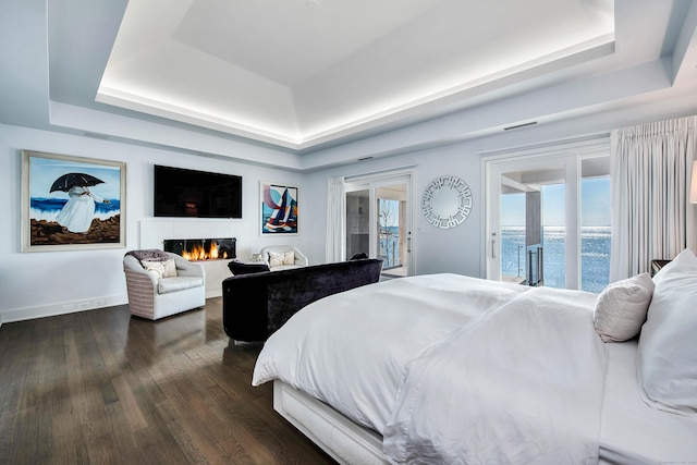 bedroom featuring a tray ceiling, access to exterior, and dark hardwood / wood-style floors