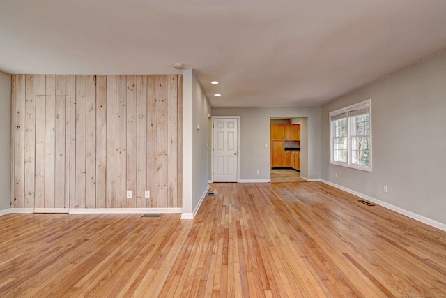 spare room featuring wood walls and light hardwood / wood-style floors