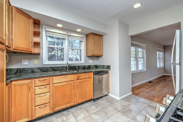 kitchen with dark stone counters, dishwasher, light tile patterned floors, and sink