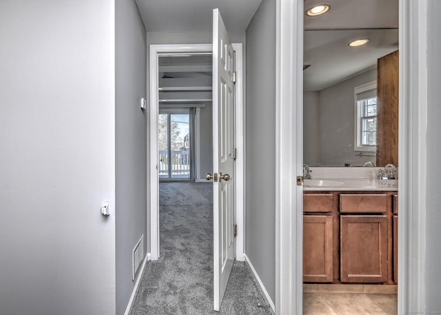 hallway with light colored carpet, a healthy amount of sunlight, and sink