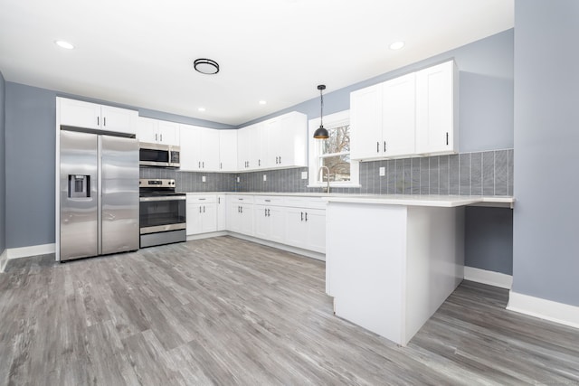 kitchen with decorative light fixtures, appliances with stainless steel finishes, white cabinetry, and light hardwood / wood-style floors