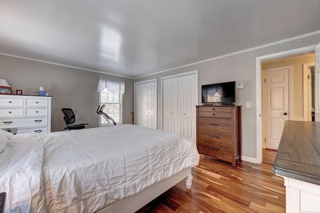 bedroom featuring ornamental molding, two closets, and light hardwood / wood-style flooring