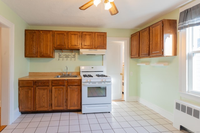 kitchen with gas range gas stove, light tile patterned floors, ceiling fan, radiator, and sink