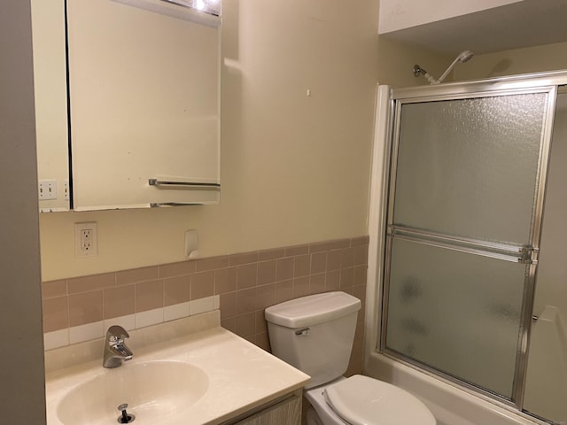 full bathroom featuring tile walls, enclosed tub / shower combo, vanity, and toilet