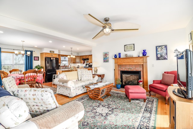 living room featuring a fireplace, ceiling fan with notable chandelier, and light hardwood / wood-style flooring