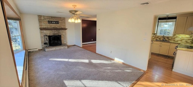 unfurnished living room featuring sink, baseboard heating, ceiling fan, and a stone fireplace