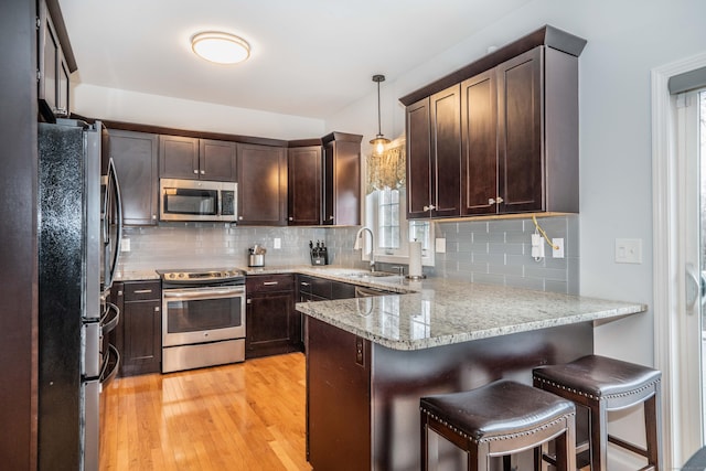 kitchen featuring kitchen peninsula, sink, hanging light fixtures, light stone countertops, and stainless steel appliances