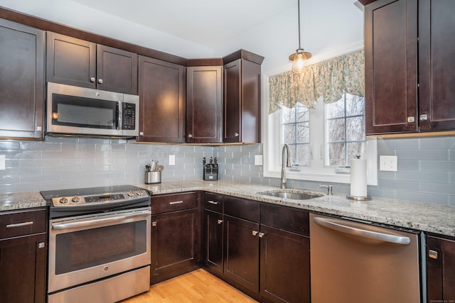 kitchen featuring stainless steel appliances, dark brown cabinets, hanging light fixtures, light stone countertops, and sink