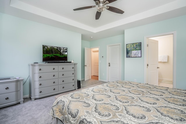 carpeted bedroom featuring ceiling fan, a tray ceiling, and ensuite bath