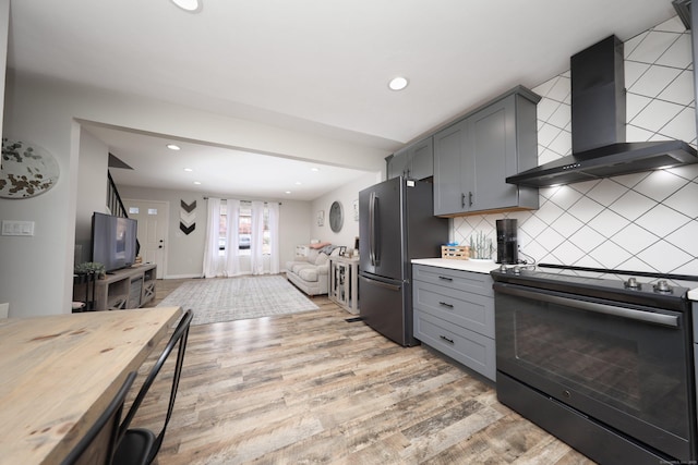 kitchen with wall chimney range hood, decorative backsplash, gray cabinetry, black / electric stove, and stainless steel fridge