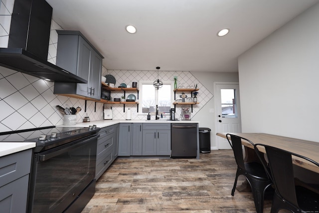 kitchen with light wood-type flooring, pendant lighting, wall chimney range hood, black appliances, and sink