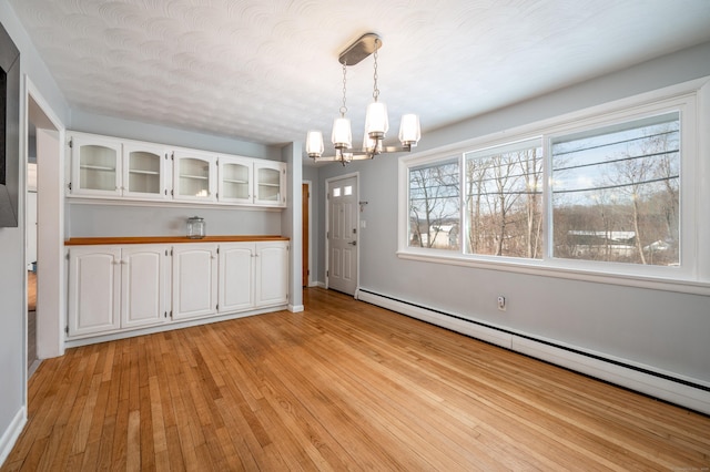 unfurnished dining area featuring a chandelier, a baseboard heating unit, light hardwood / wood-style floors, and a textured ceiling