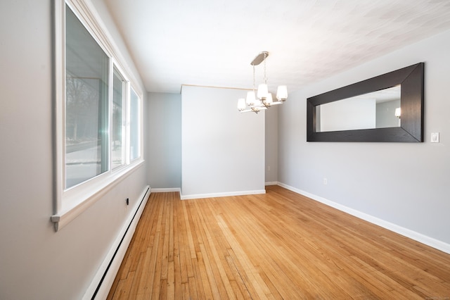 unfurnished room featuring baseboard heating, an inviting chandelier, and light hardwood / wood-style floors