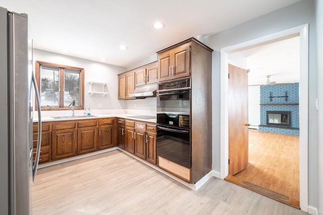 kitchen featuring sink, black appliances, a fireplace, and light hardwood / wood-style floors