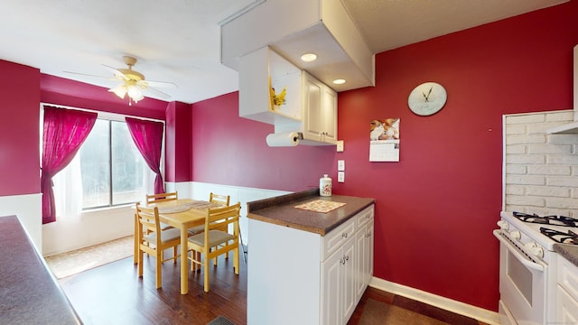 kitchen with dark wood-type flooring, ceiling fan, white cabinetry, and gas range gas stove