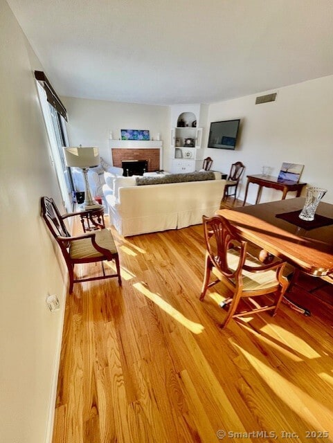 dining room featuring a brick fireplace, wood finished floors, visible vents, and baseboards