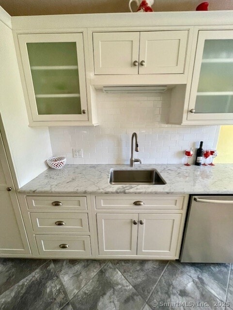 kitchen with stainless steel dishwasher, a sink, glass insert cabinets, and light stone countertops