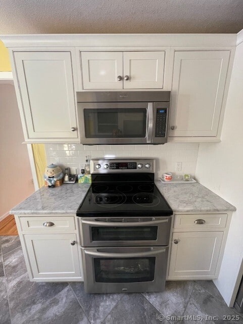 kitchen with stainless steel appliances, light stone countertops, white cabinetry, and decorative backsplash