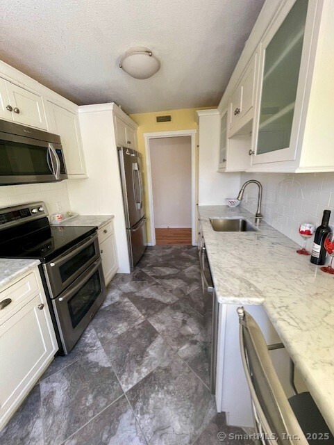 kitchen with light stone counters, glass insert cabinets, stainless steel appliances, and a sink