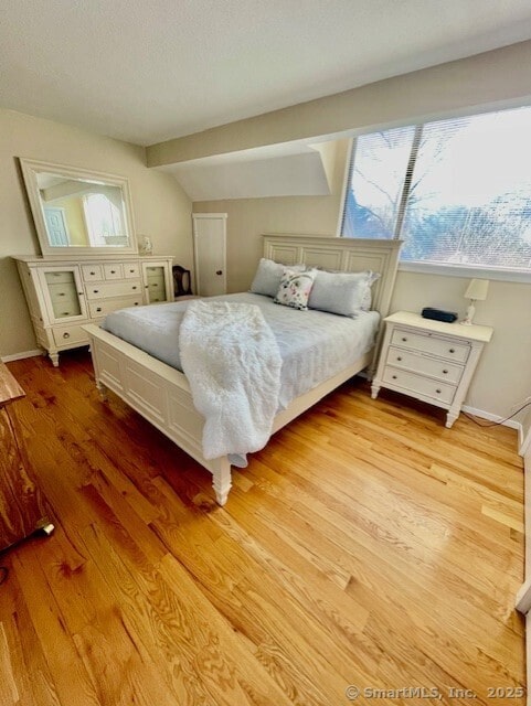 bedroom with light wood finished floors, baseboards, and vaulted ceiling