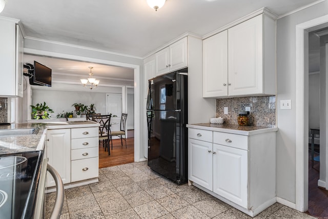 kitchen with electric stove, decorative light fixtures, black refrigerator, an inviting chandelier, and white cabinetry