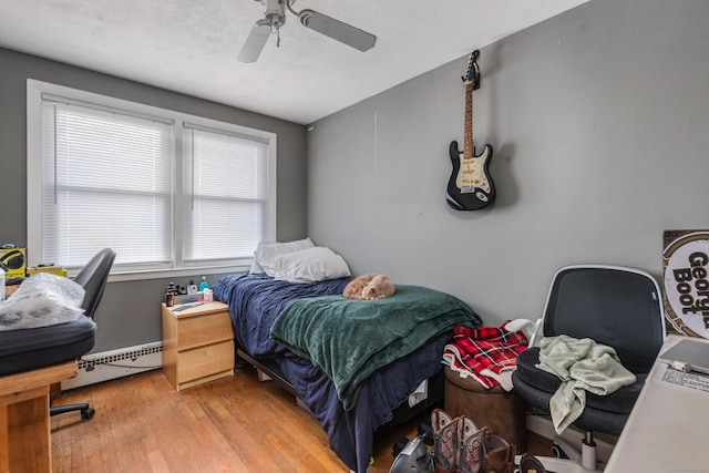 bedroom featuring ceiling fan, light hardwood / wood-style floors, and a baseboard heating unit