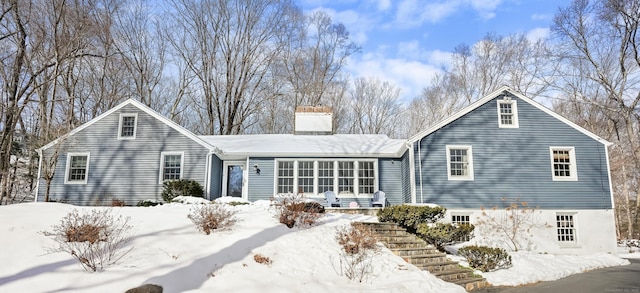 snow covered back of property featuring a chimney