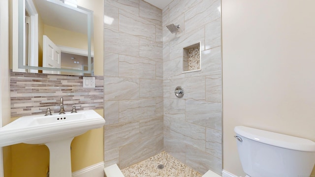 bathroom with a tile shower, sink, decorative backsplash, and toilet