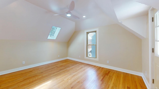 additional living space featuring ceiling fan, vaulted ceiling with skylight, and light wood-type flooring