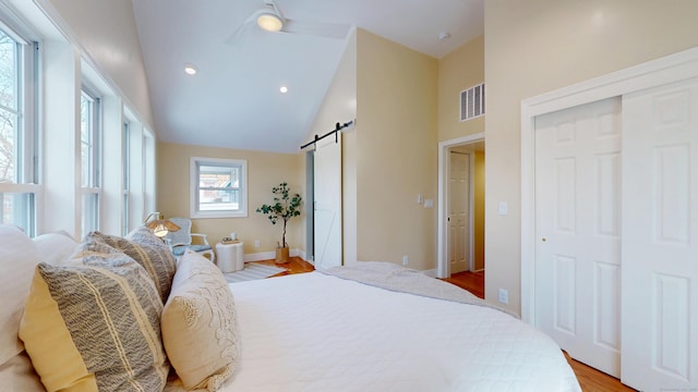 bedroom with a barn door, high vaulted ceiling, and light wood-type flooring