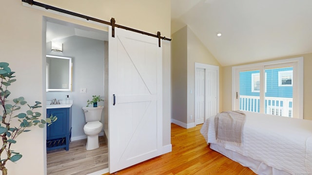 bedroom featuring ensuite bath, light hardwood / wood-style flooring, access to outside, vaulted ceiling, and a barn door