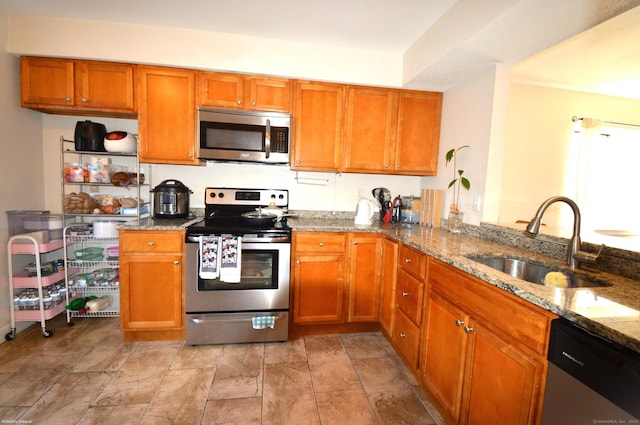 kitchen featuring kitchen peninsula, light stone countertops, appliances with stainless steel finishes, and sink