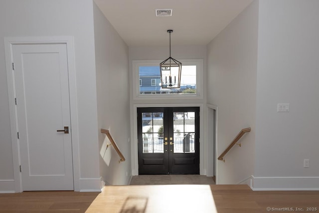 entryway featuring a chandelier, wood finished floors, a towering ceiling, visible vents, and french doors